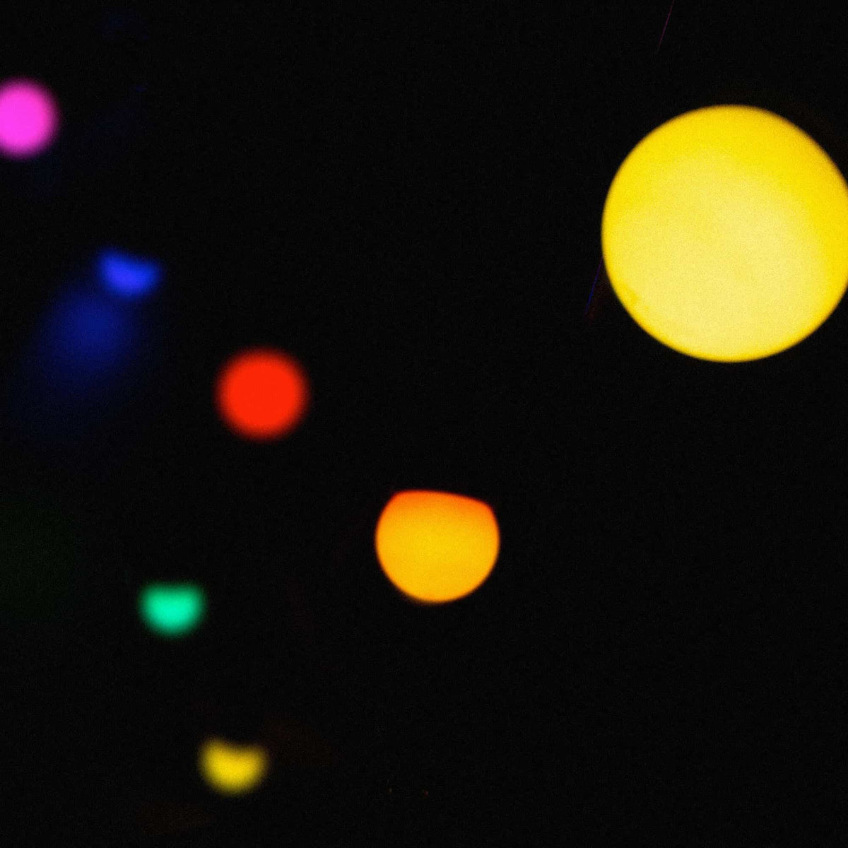 Guirlande lumineuse extérieure multicolore floue dans la nuit, avec des points lumineux jaunes, orange, rouges, verts, bleus et violets sur fond sombre.