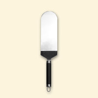 Grande spatule à poisson en inox avec manche noir, présentée sur fond beige.