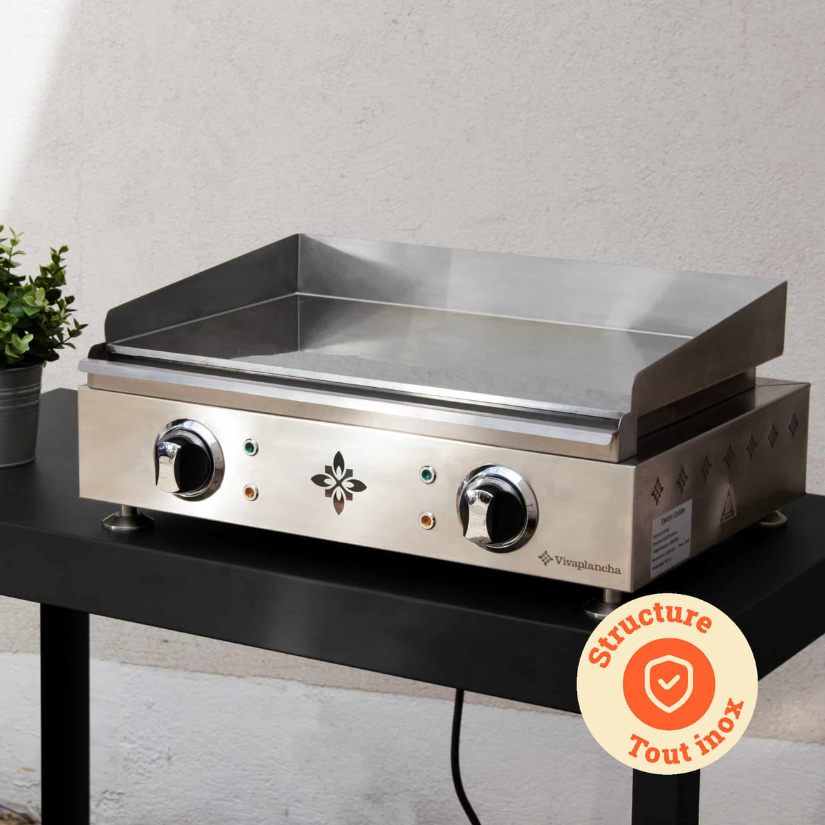 Plancha Vivaplancha colocada sobre uma mesa exterior, com a sua estrutura totalmente em inox em destaque e um crachá “Estrutura totalmente em inox” exibido num círculo laranja.